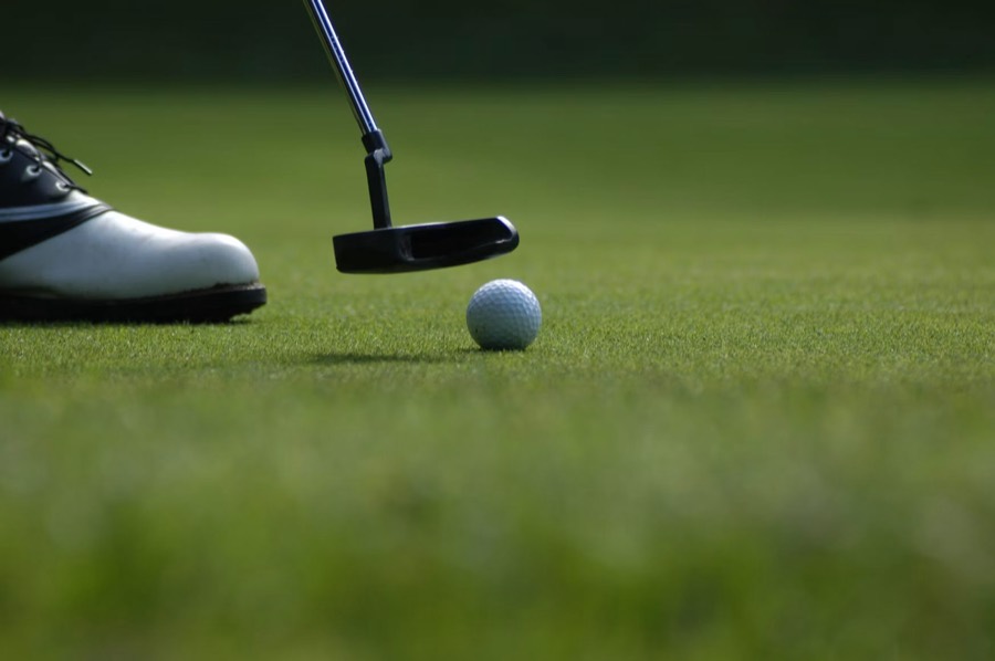 A golfer lining up a putt on a quiet green in low evening light.