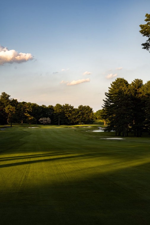 Long shadows stretch across a fairway in warm late-afternoon light.